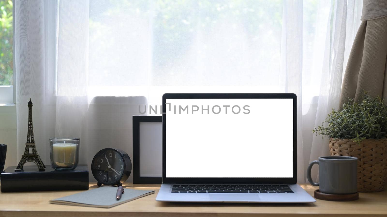 Front view laptop computer with white screen, potted plant, coffee cup and picture frame on wooden table.