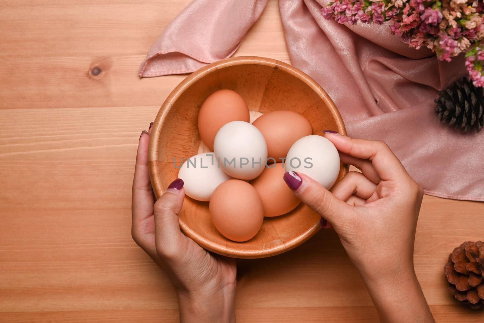 Overhead view young woman arranging eggs into wooden bowl, preparing for Easter celebration.