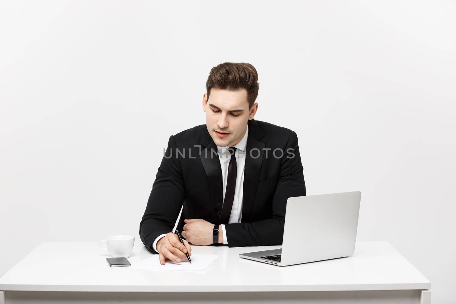 Concentrated young businessman writing documents at office desk