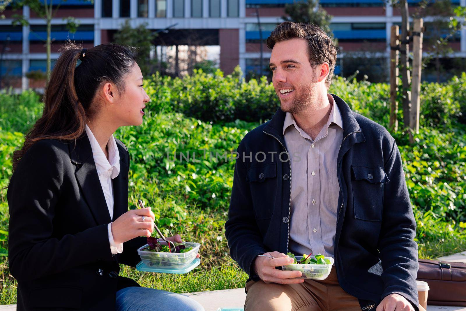 coworkers chatting and eating a salad during a work break in the park next to the office, concept of healthy fast food at work