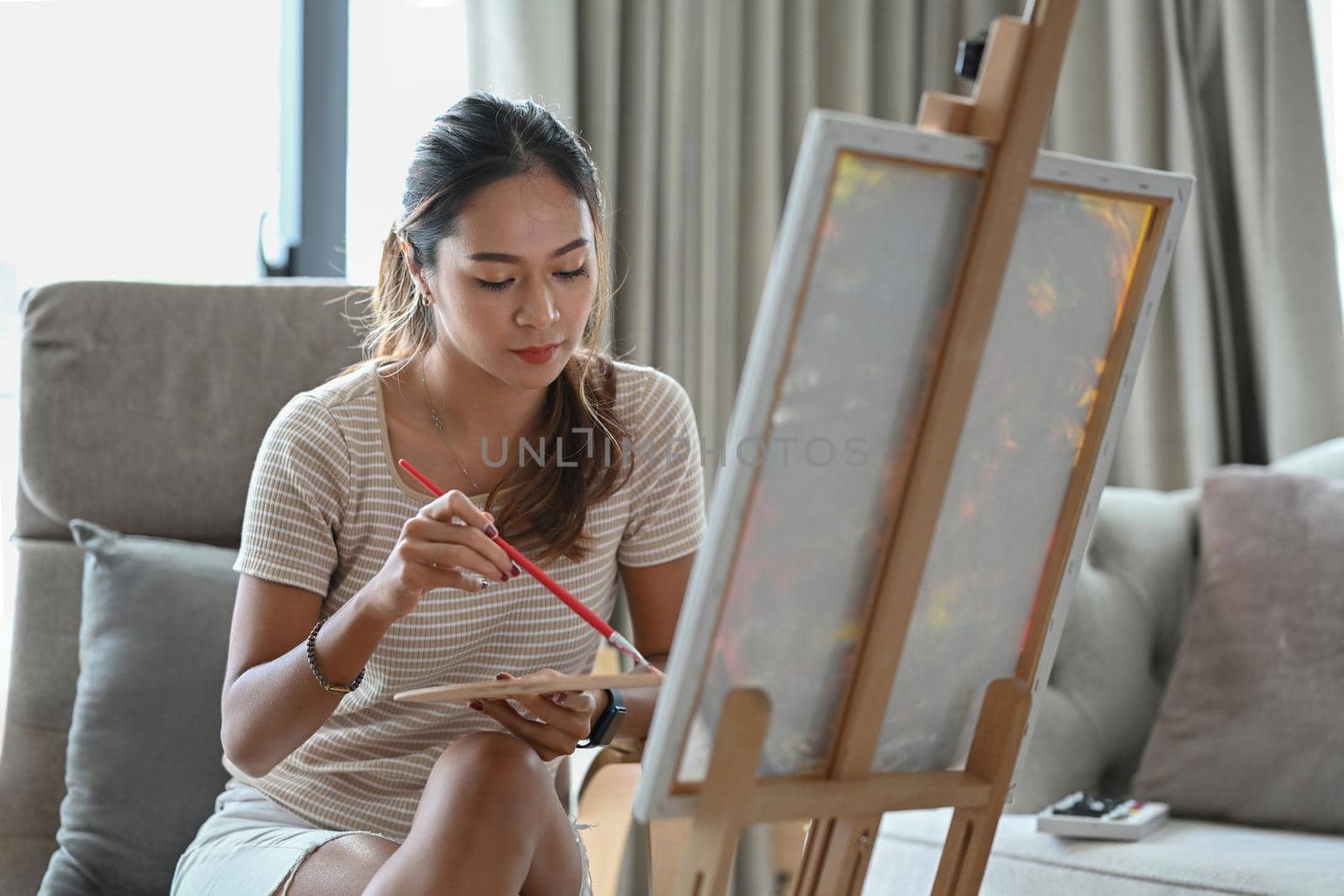 Attractive Asian woman painting on canvas at home. Hobby and leisure concept.