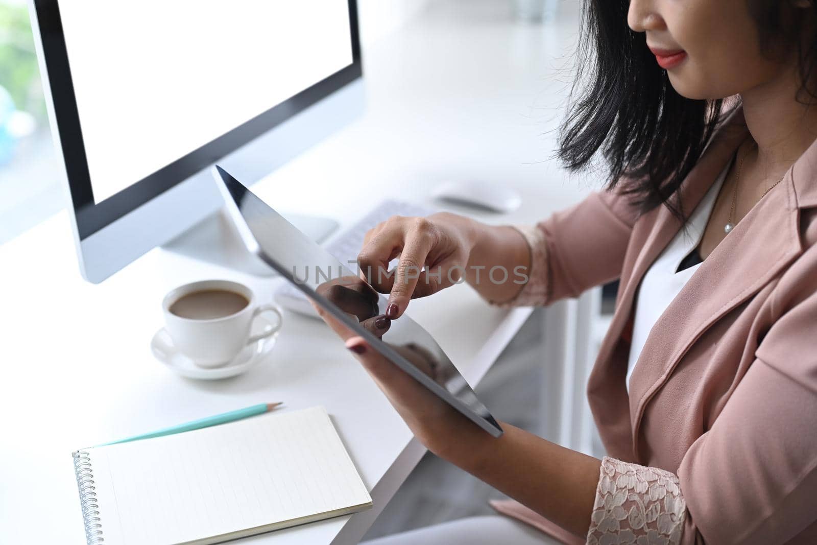 Asian businesswoman sitting in modern workplace and using digital tablet.