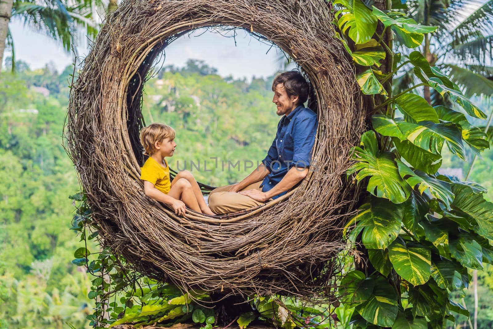 Bali trend, straw nests everywhere. Child friendly place. Happy family enjoying their travel around Bali island, Indonesia. Making a stop on a beautiful hill. Photo in a straw nest, natural environment. Lifestyle. Traveling with kids concept. What to do with children.