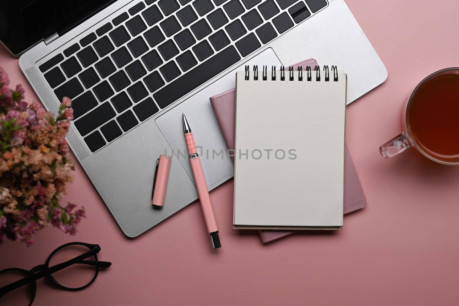 Feminine workplace with laptop computer, notebook, coffee cup an glasses on pink background.