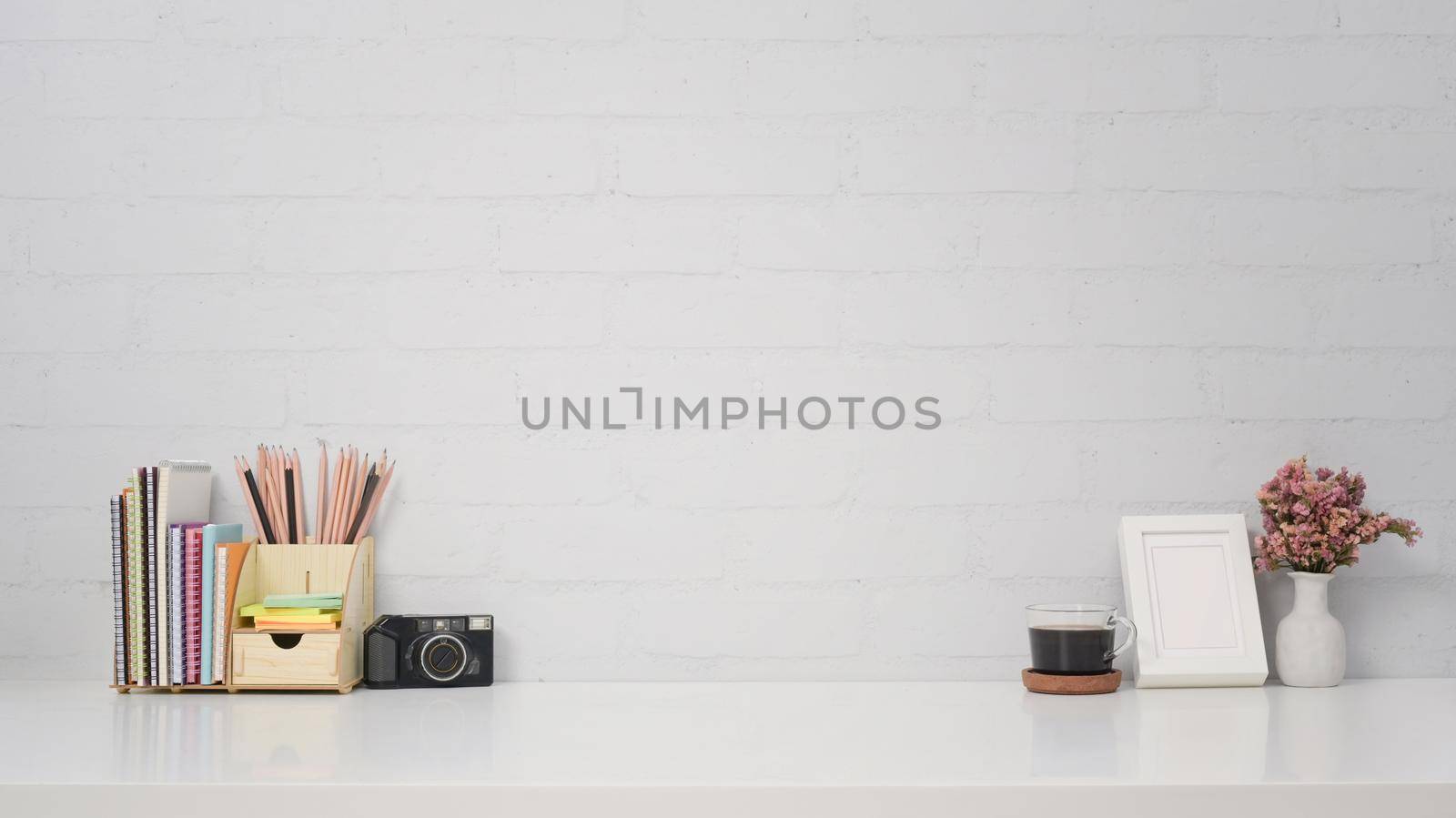 Stylish workplace with camera, coffee cup, picture frame and stationery on white table.
