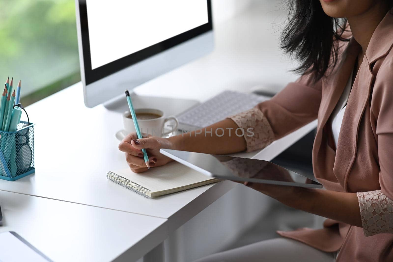 Young businesswoman holding digital tablet and writing information on notebook.