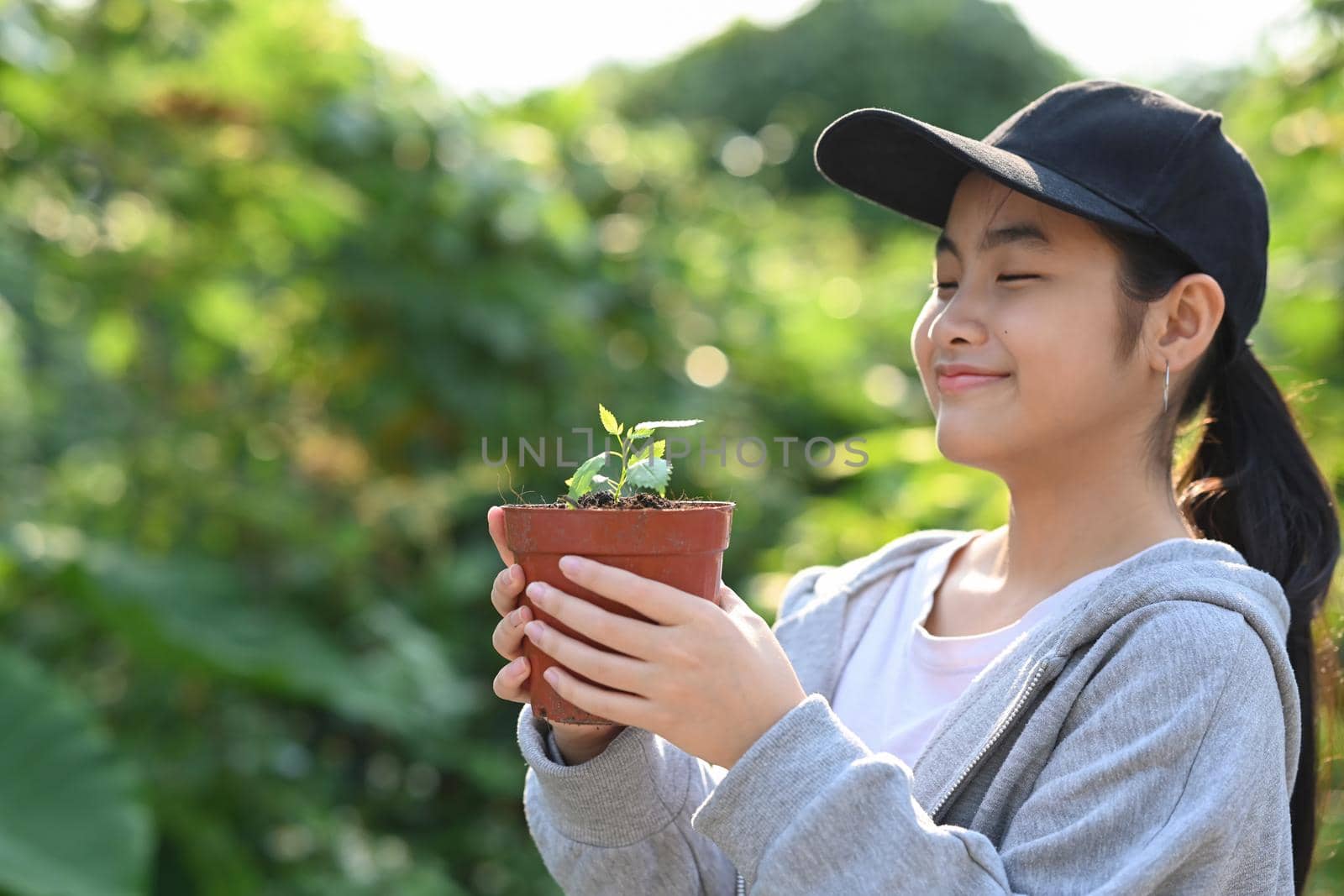 Cute asian girl closed eyes while holding a plant in her hands. Saving the world, earth day concept.