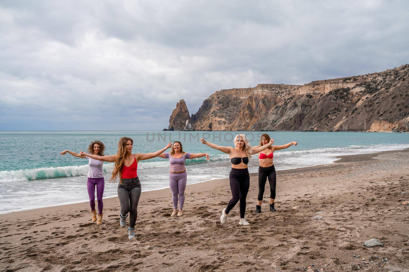 A group of five female friends are doing exercises on the beach. Beach holiday concept, healthy lifestyle.