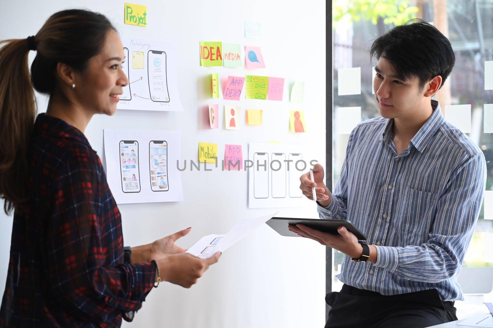 Two website developer presenting and testing mobile app interface design on whiteboard at creative office.