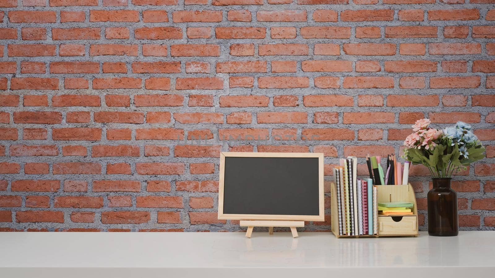 Blank small blackboard and supplies on white table against brick wall with copy space for your text message or product isolated.
