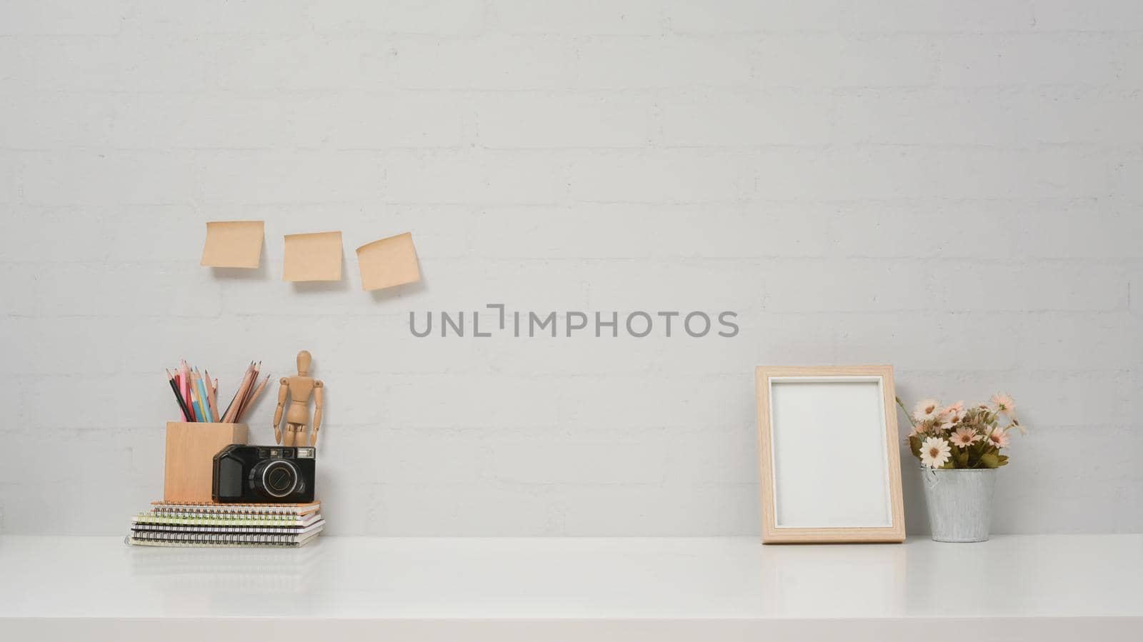 Contemporary workspace with camera, picture frame and flower pot on white table against brick wall.