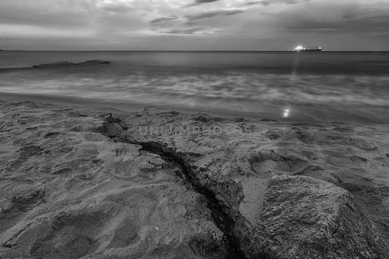 Amazing seascape with a light ray from the ship and a small brook flowing into the sea. Black and white
