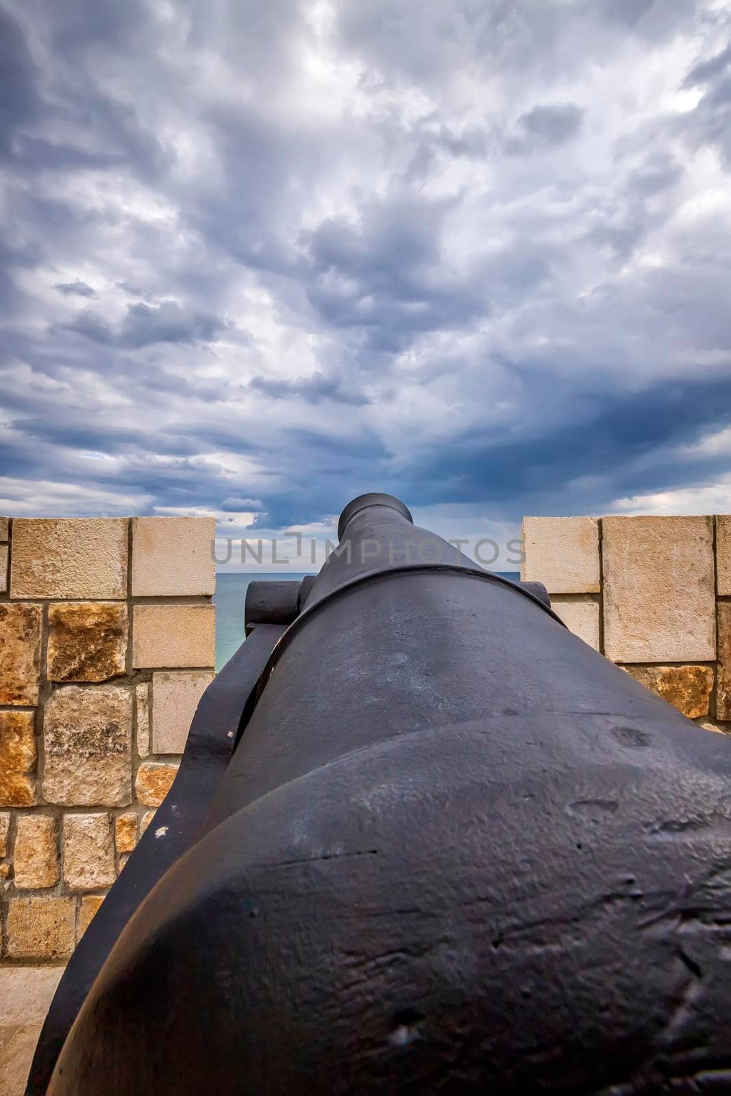Old iron cannon pointing through an opening in a castle rampart. by EdVal