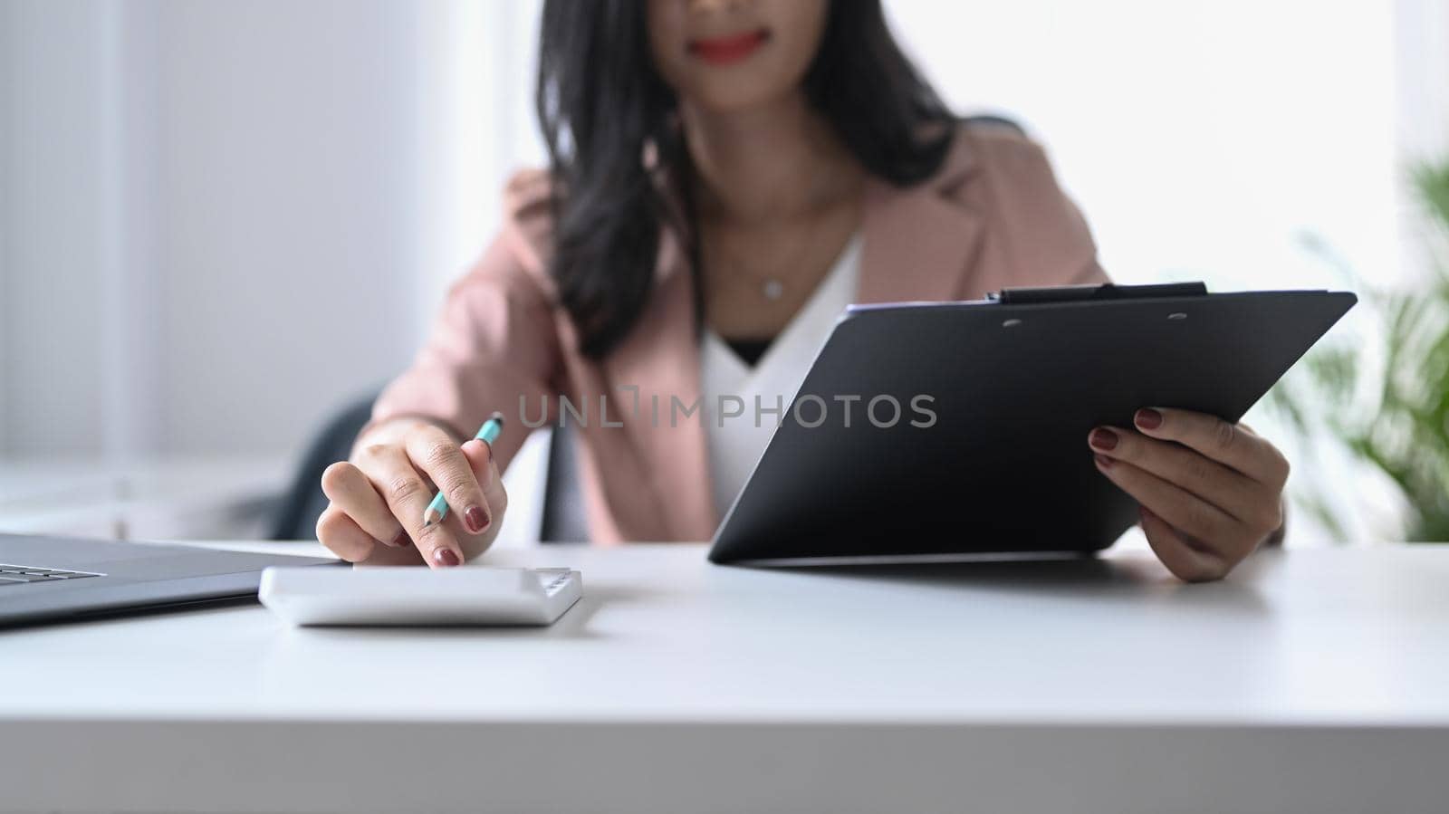 Focused professional female accountant is using calculator at office desk.