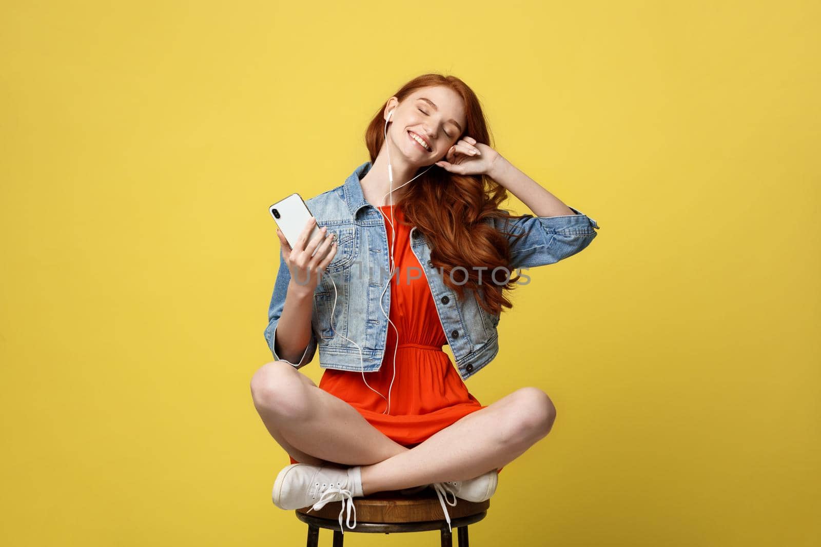 Lifestyle, Music, Technology concept: Young beautiful caucasian woman listening music with headphones and smart phone hand hold, dancing, eyes closed smiling, Isolated on yellow vivid background. by Benzoix