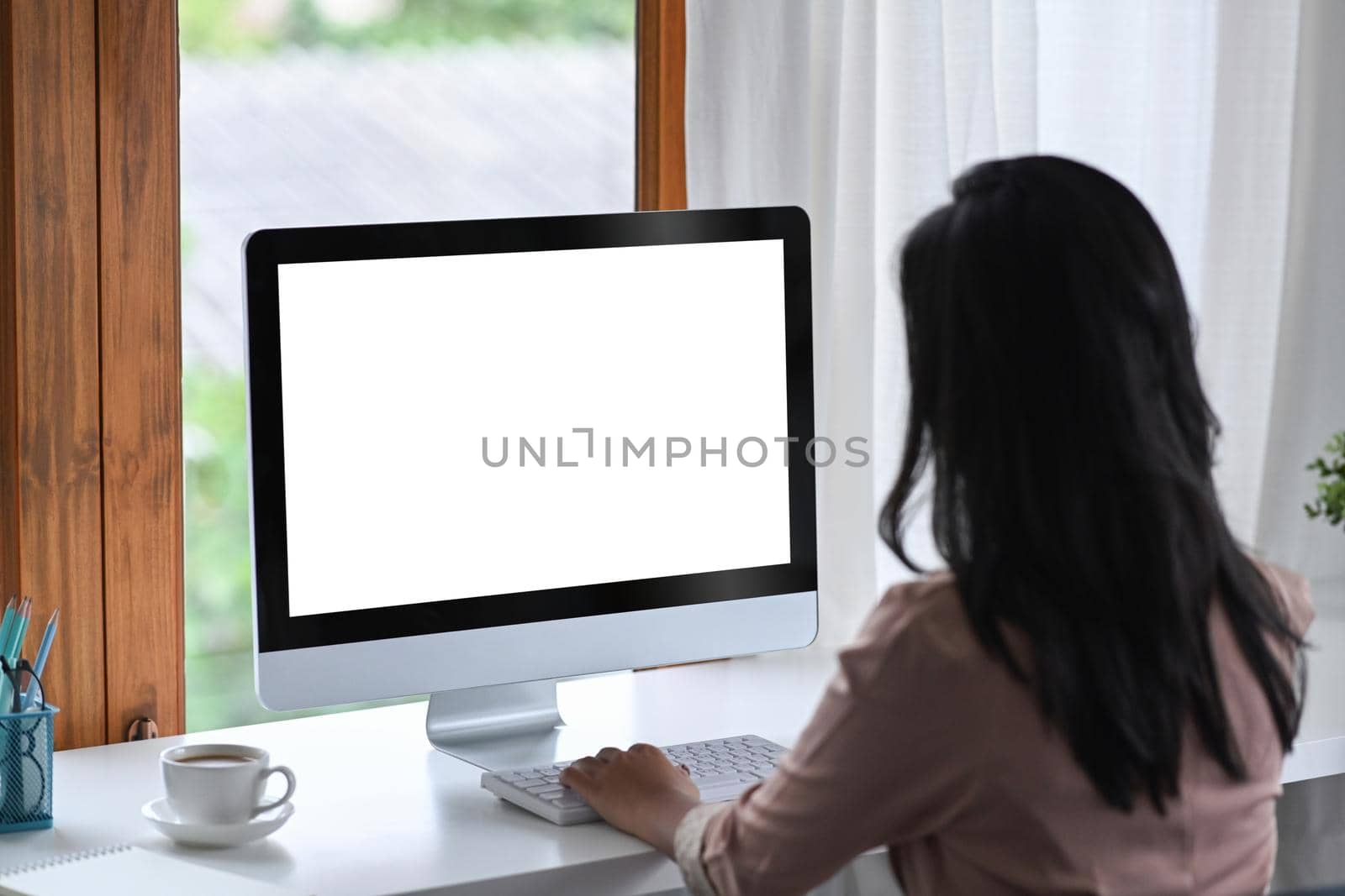Rear view of businesswoman using computer at bright modern workplace.
