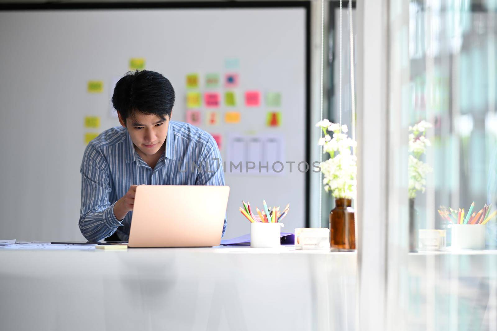 Young asian male web developer working on mobile application software design project at modern workplace.