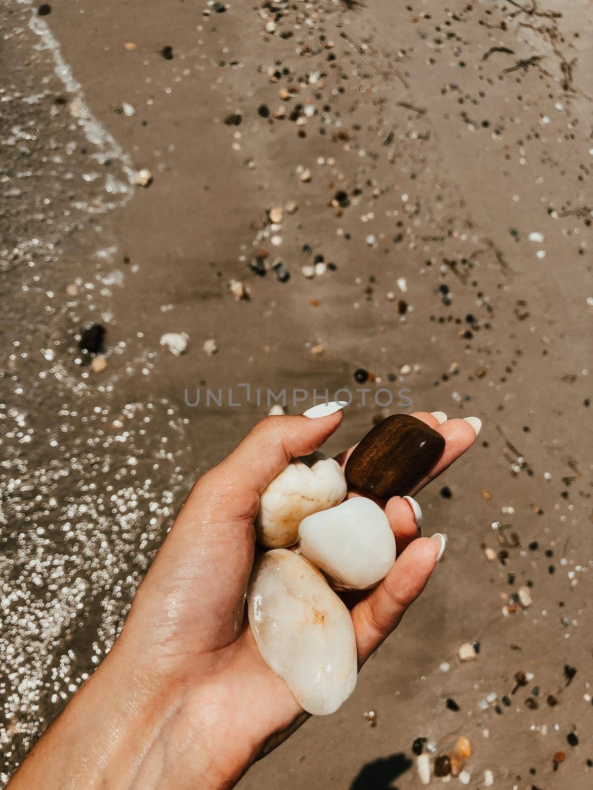 Woman hand manicure holding white beautiful stones above sea sandy summer beach. Natural background. Girl keep on palm sea pebbles. Template free space pattern wallpaper mockup. Summer background.
