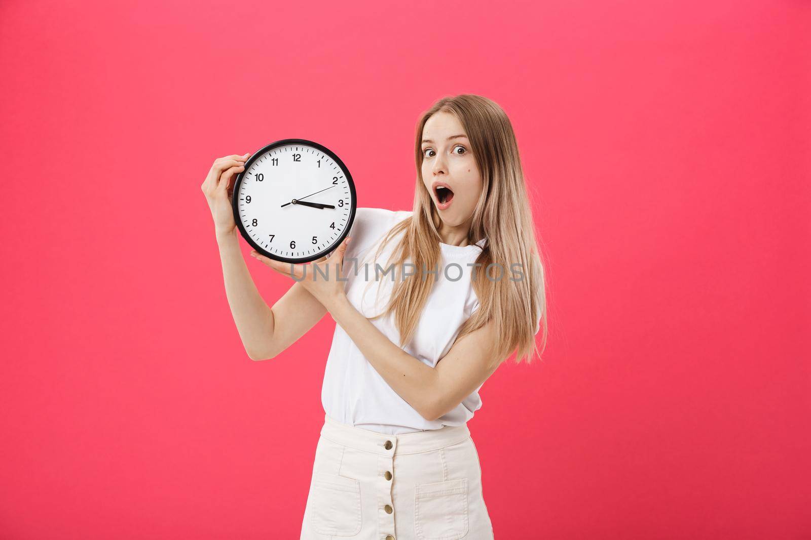 Amazed woman holding clock. Surprised woman in white t-shirt holds black clock. Retro style. Saving time concept. Summer sale. Discount. Isolated on pink background. by Benzoix