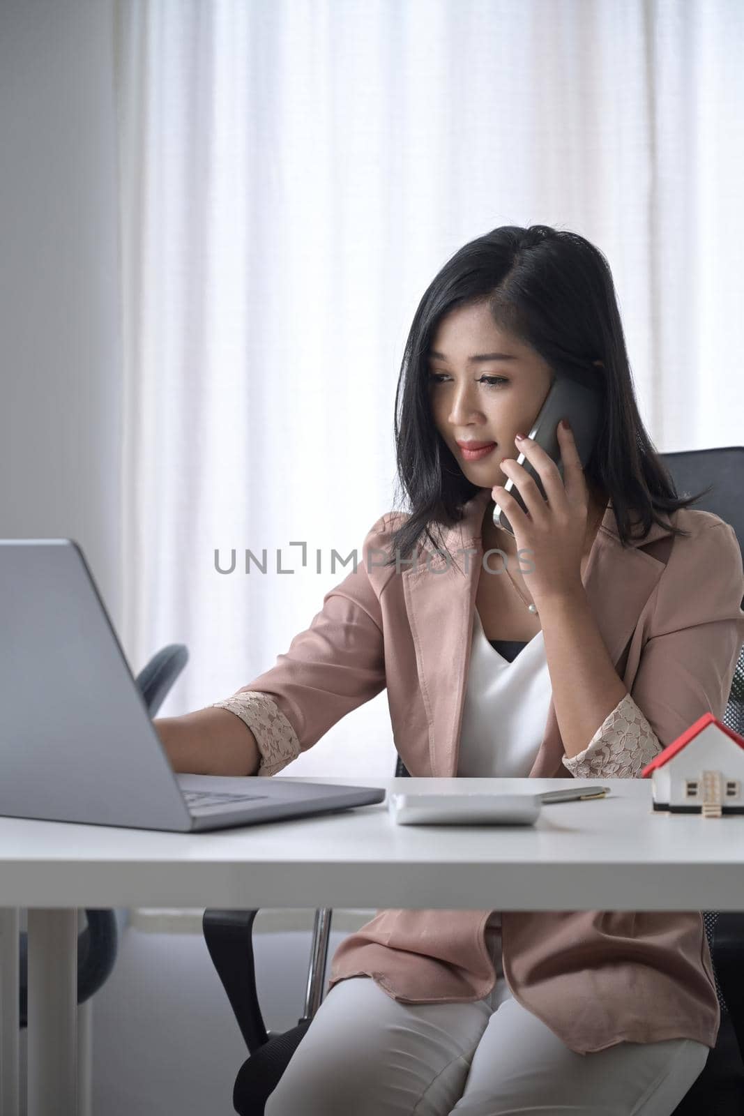 Busy businesswoman using laptop computer and talking on mobile phone.