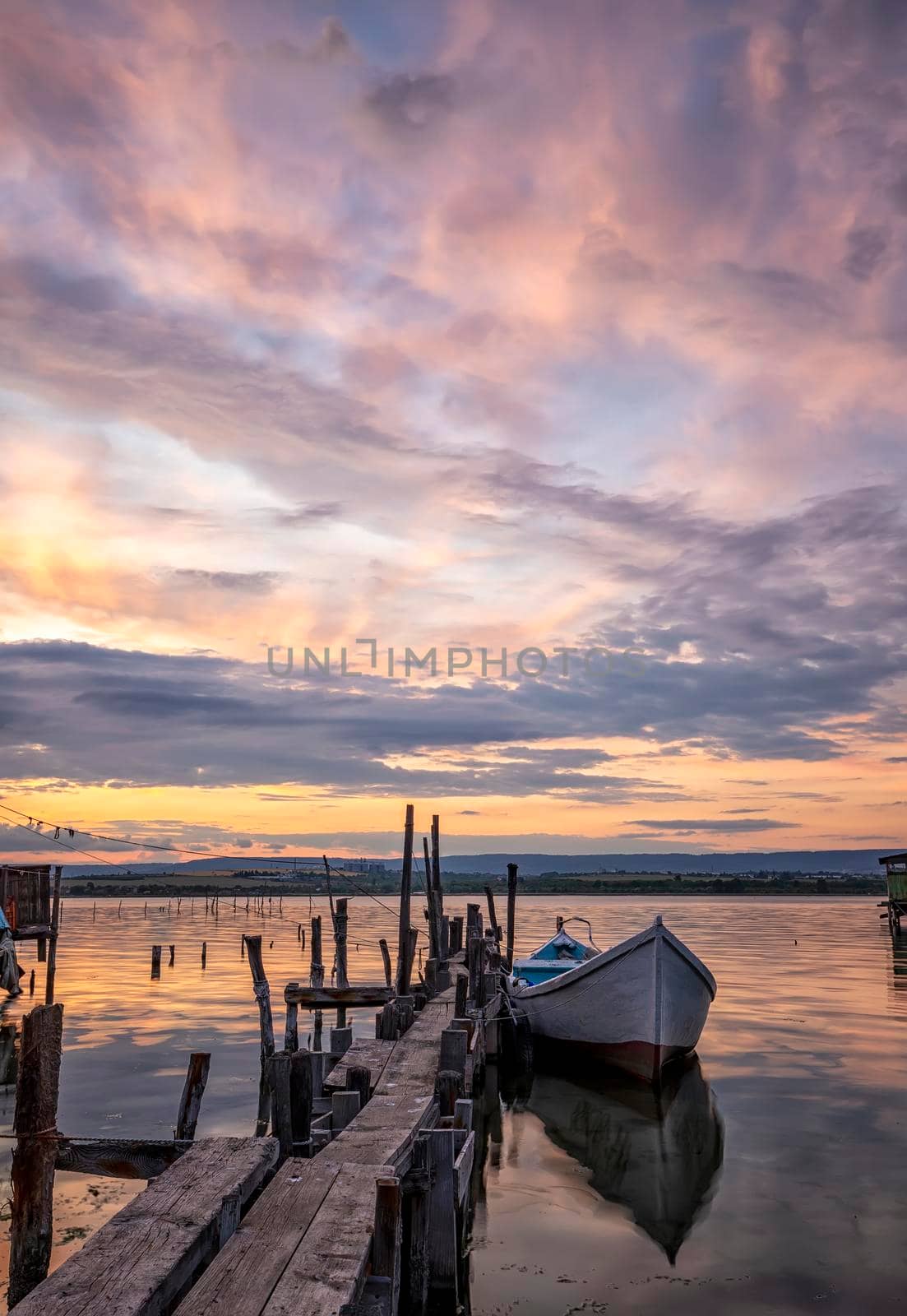 mood and tranquility at a lake coast with a boat at a wooden pier. Vertical view by EdVal