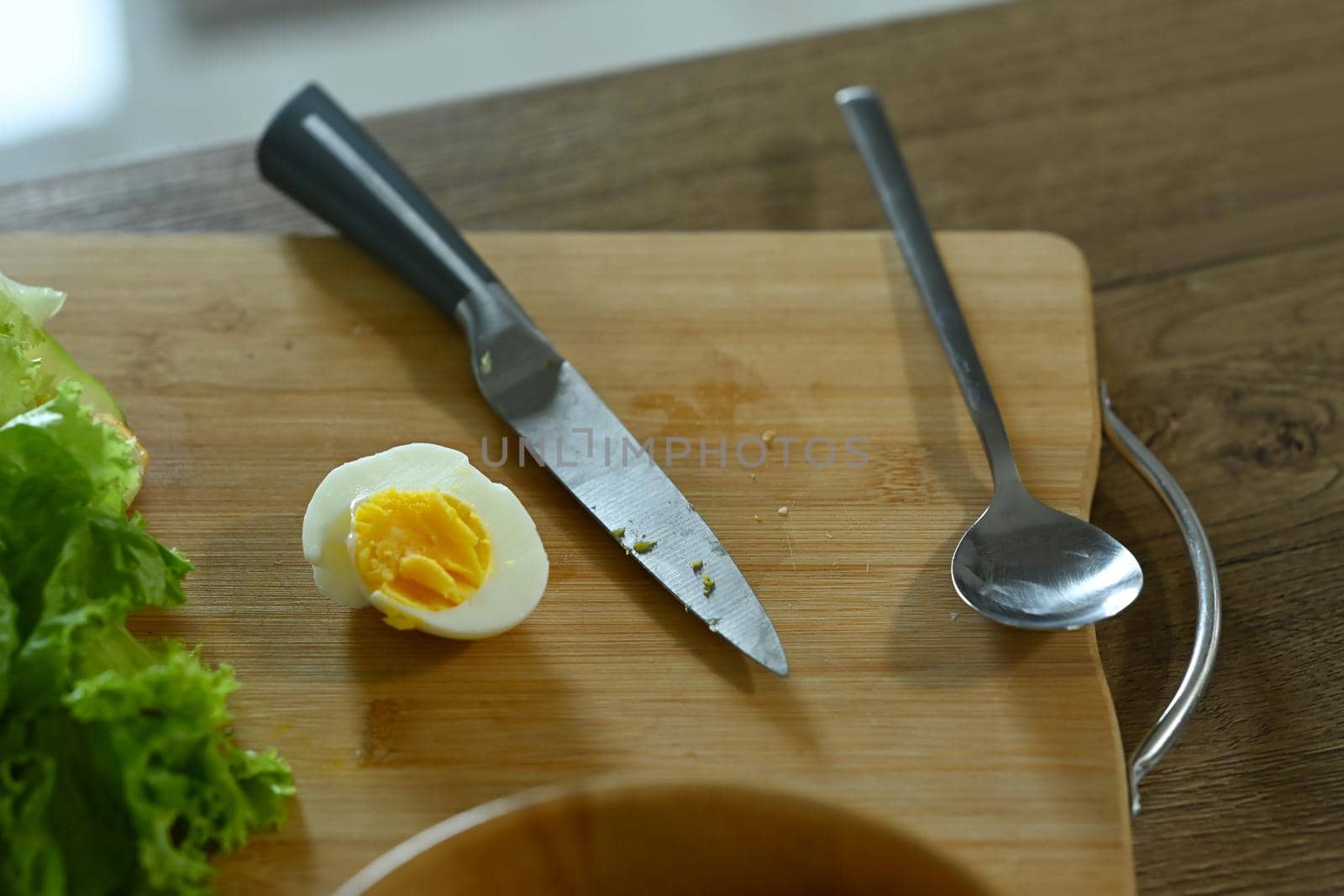Above view boiled egg, knife and .fresh lettuces on wooden table in kitchen.