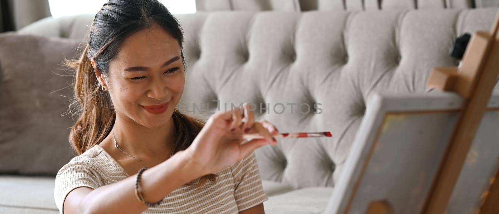 Attractive woman holding paintbrush enjoy creating artwork at home.