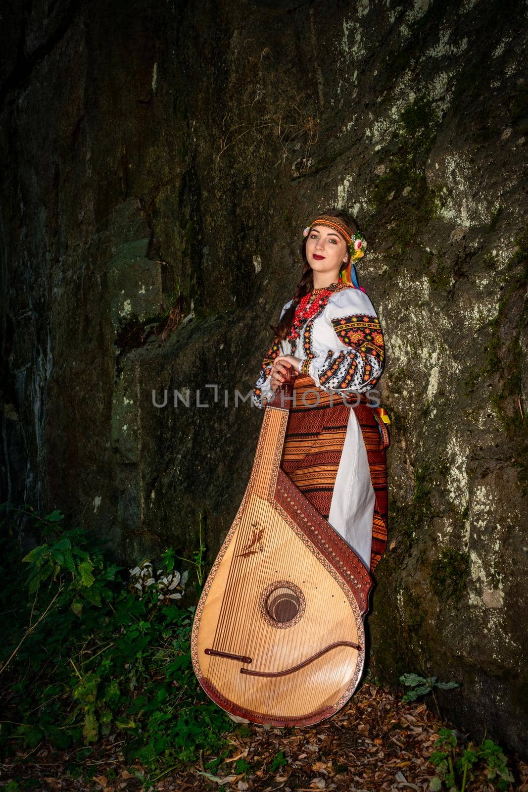 A Ukrainian musician in national clothes stands with a bandura leaning on a rock.