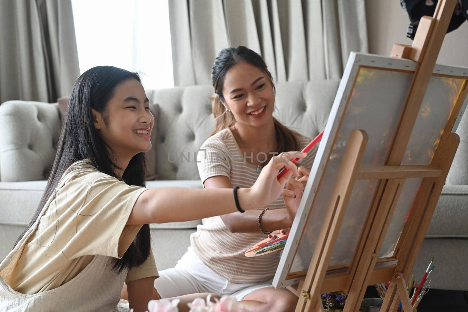 Cheerful asian girl having fun painting with her mother at home.