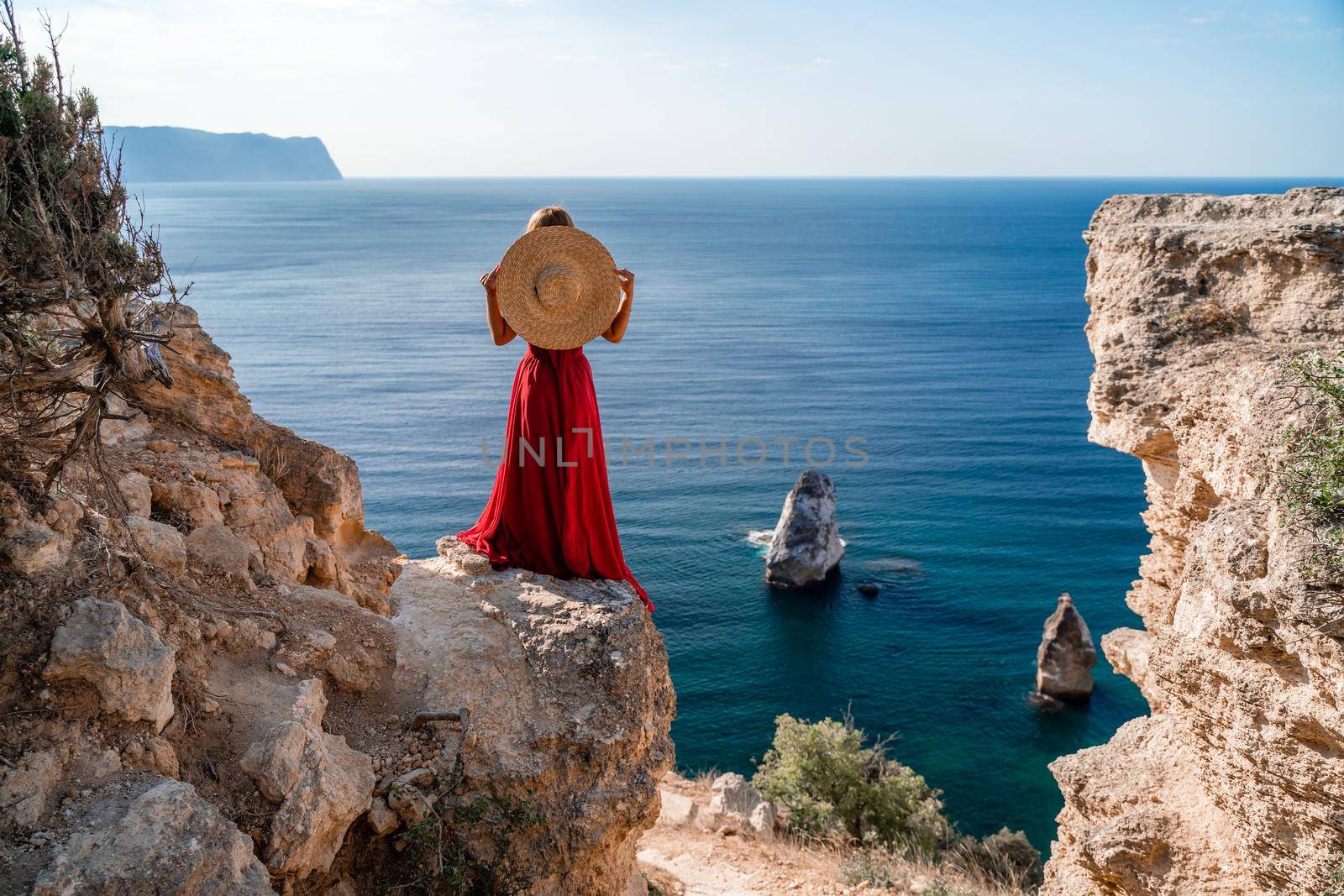 A woman in a flying red dress fluttering in the wind and a straw hat against the backdrop of the sea