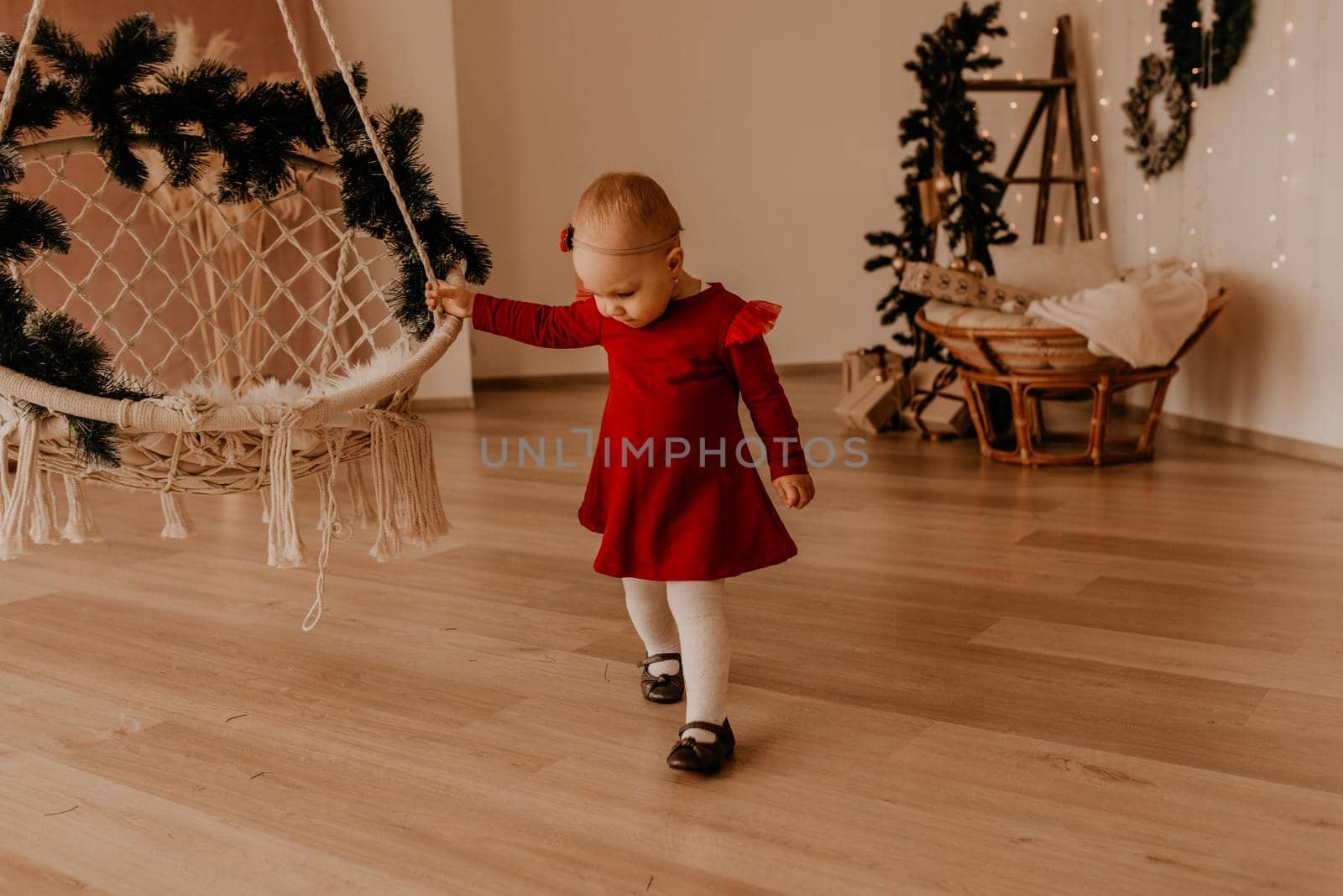 little girl in red dress runs apartment style light minimalism. child stands at white wall with garlands Christmas tree with wrapped gifts. Christmas.New Year interior.Valentine Day celebration