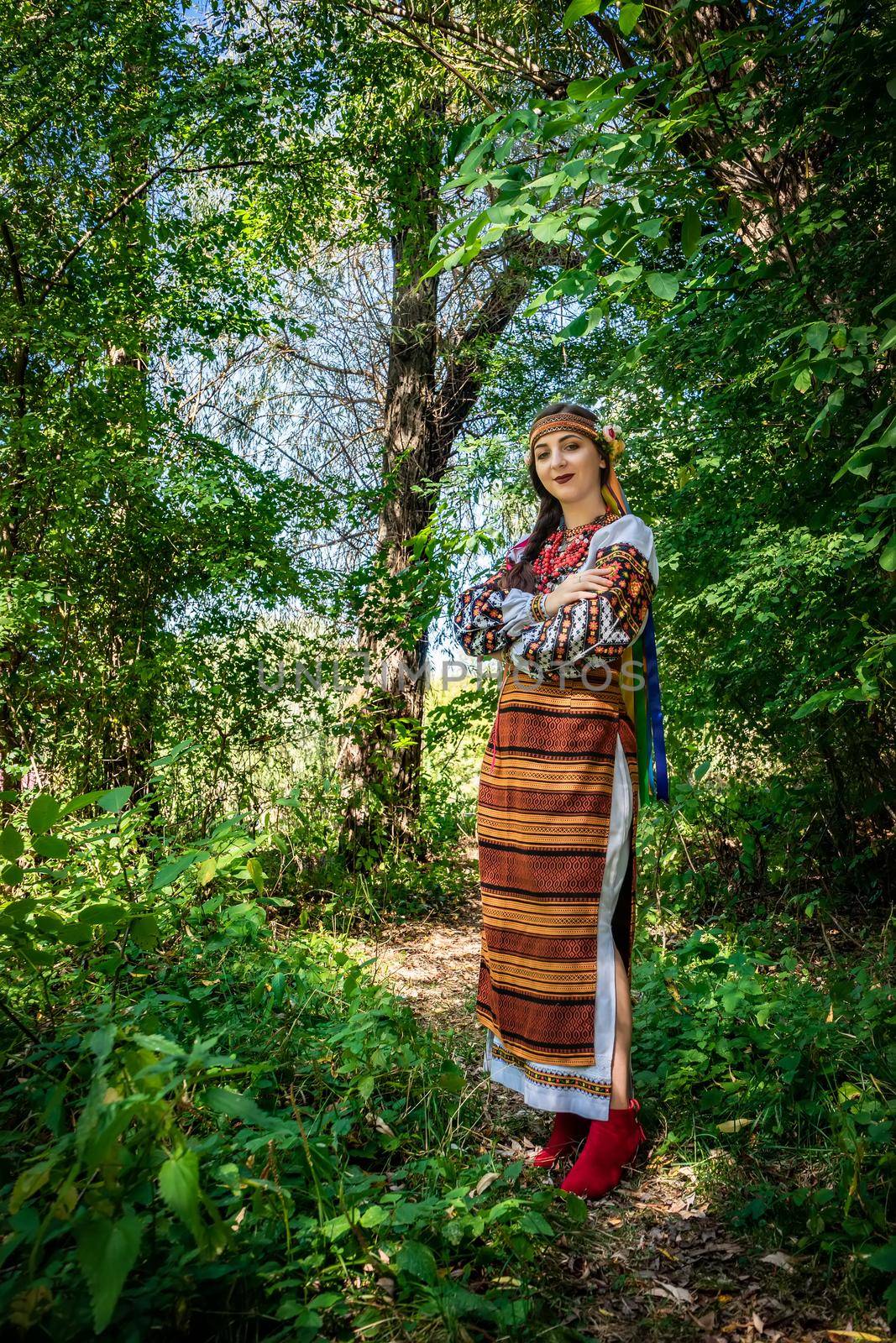 Ukrainian girl in national Ukrainian dress stands on a path in the woods.