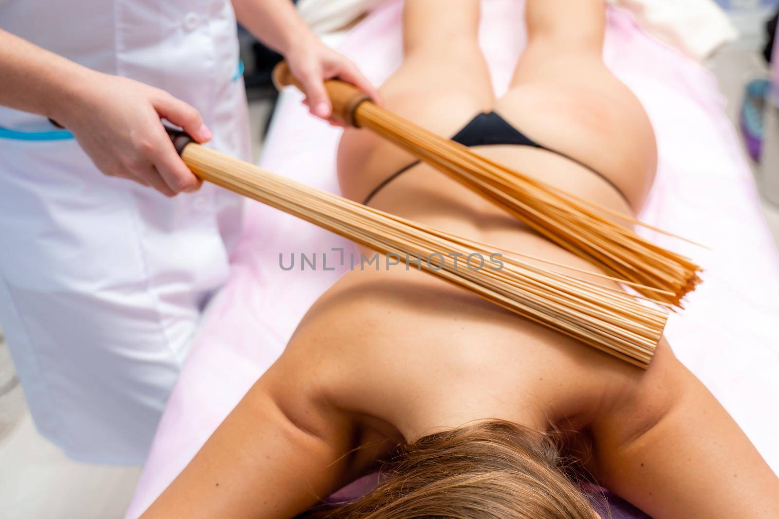 Woman masseuse doing double samurai massage with bamboo brooms in spa. Relaxing massage concept.