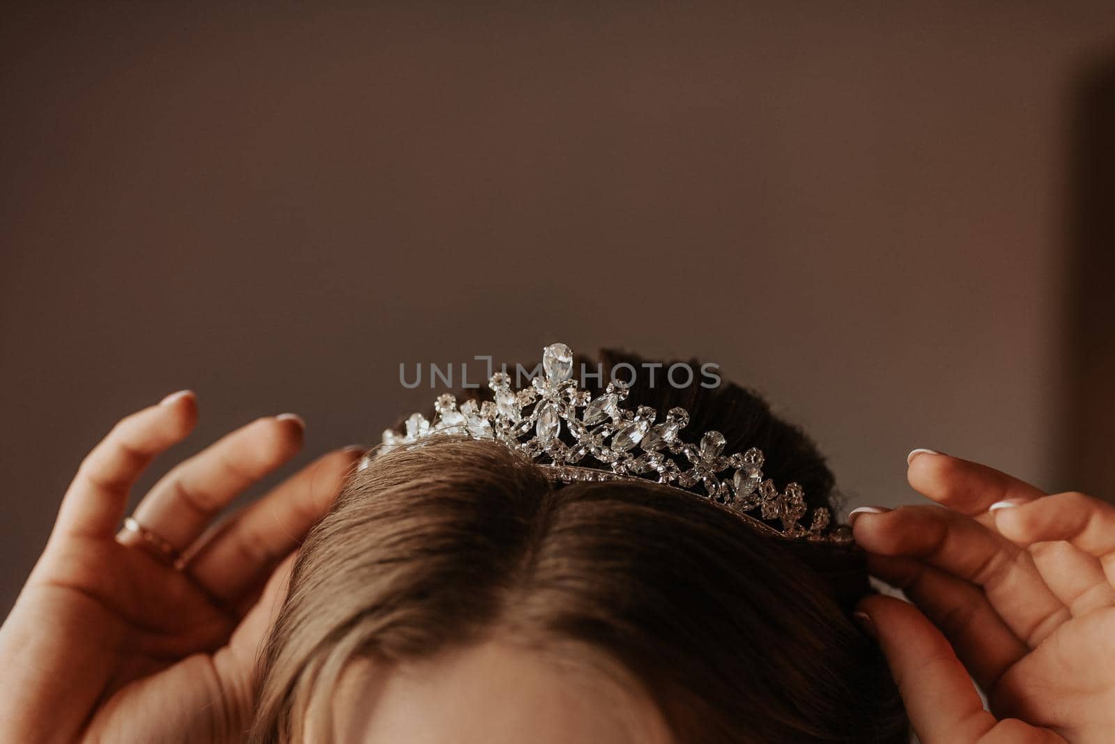 the girl holds on her head a tiara crown decorated with precious stones, young woman bride straightens accessories on her head and ears