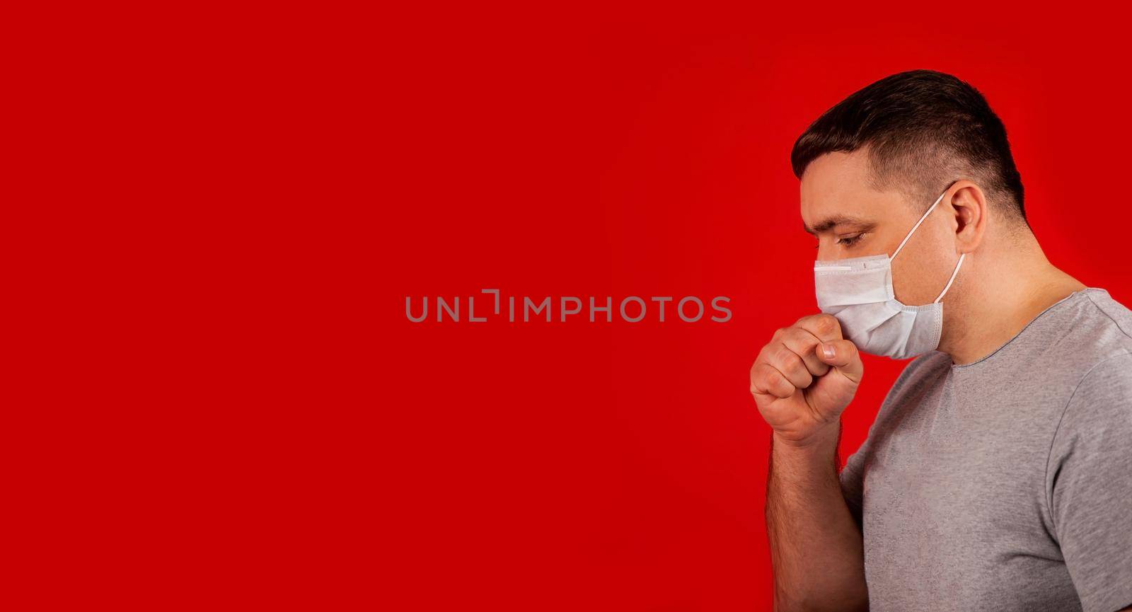 Portrait of a young sick man in a medical protective mask coughing and feeling ill. Sick man sick with chest pain. Symptoms of the pandemic coronavirus COVID-19, influenza, colds, or pneumonia