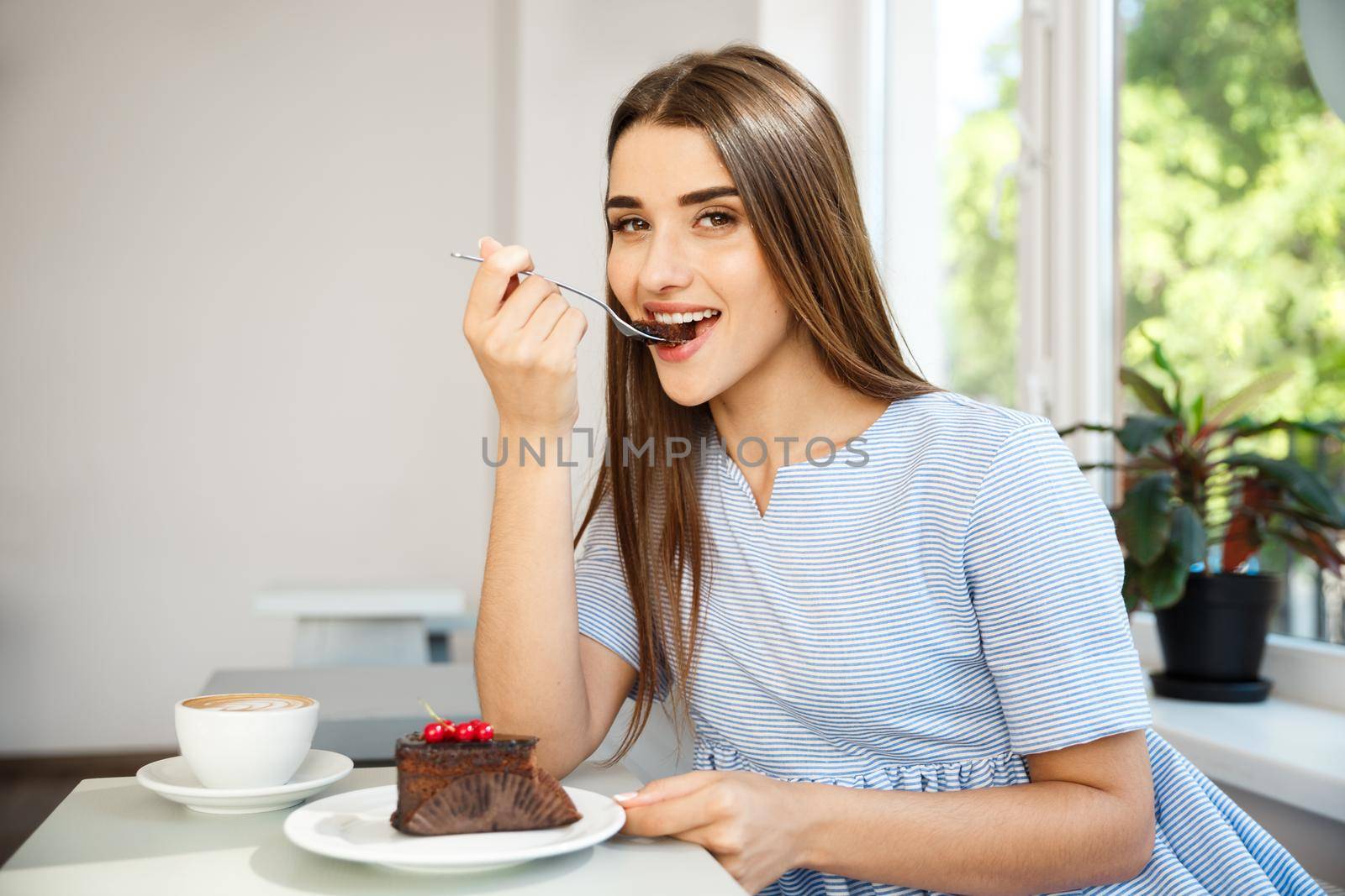 Young attractive Caucasian lady enjoy eating chocolate cake with hot coffee in modern coffee shop at noon. by Benzoix