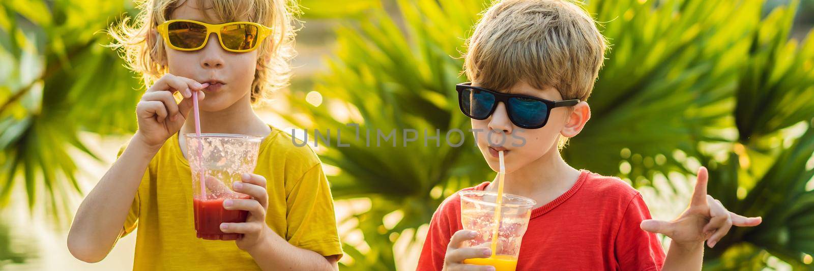 BANNER, LONG FORMAT Two boys drink healthy smoothies against the backdrop of palm trees. Mango and watermelon smoothies. Healthy nutrition and vitamins for children by galitskaya