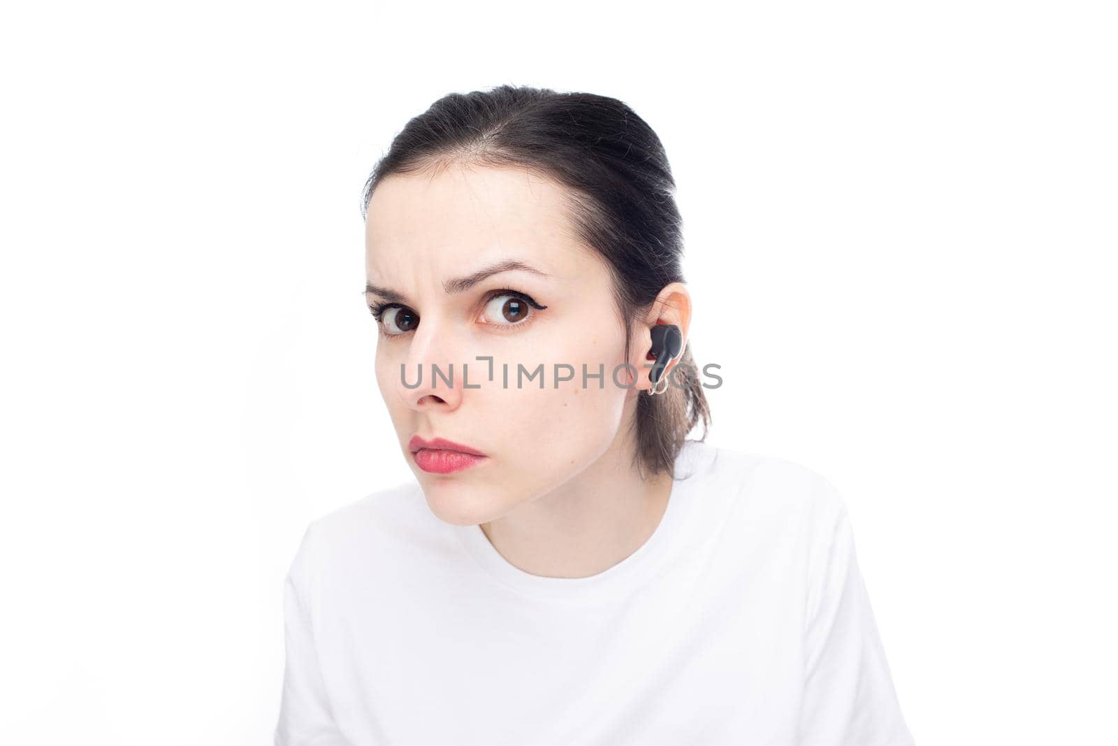 emotional woman in a white t-shirt with a small earpiece in her ear, white studio background. High quality photo