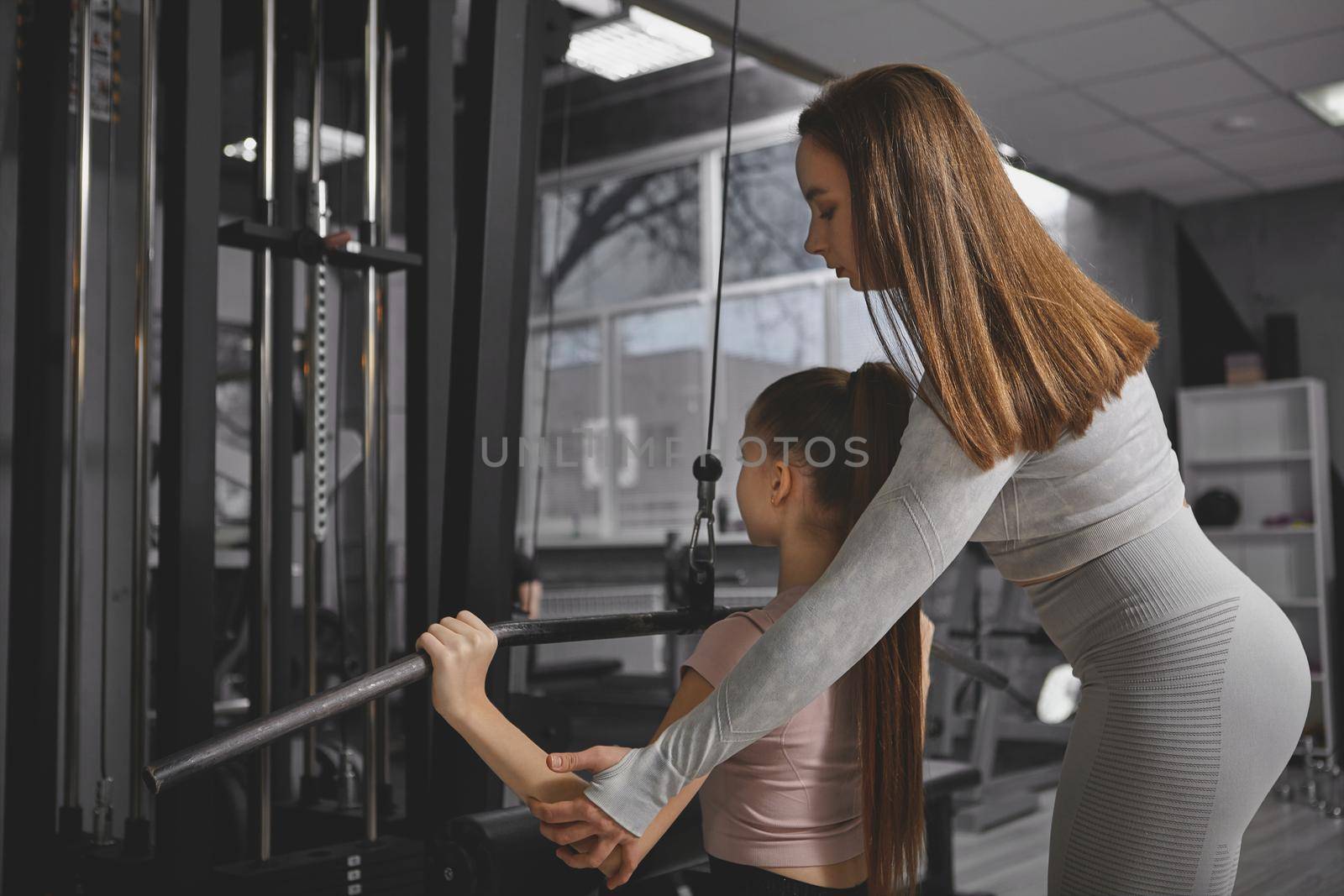 Rear view shot of personal trainer helping teenage girl exercise on lat pull down gym machine