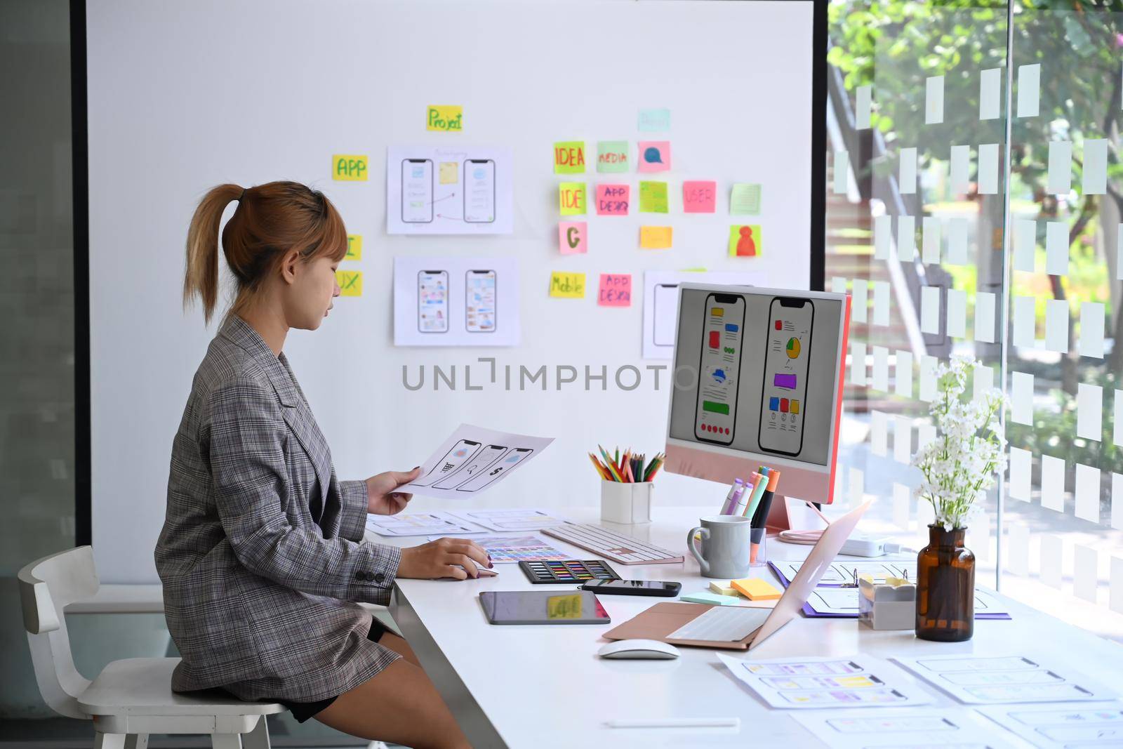 Focussed female web designer is planning, drawing application development prototype wireframe for mobile phone application.
