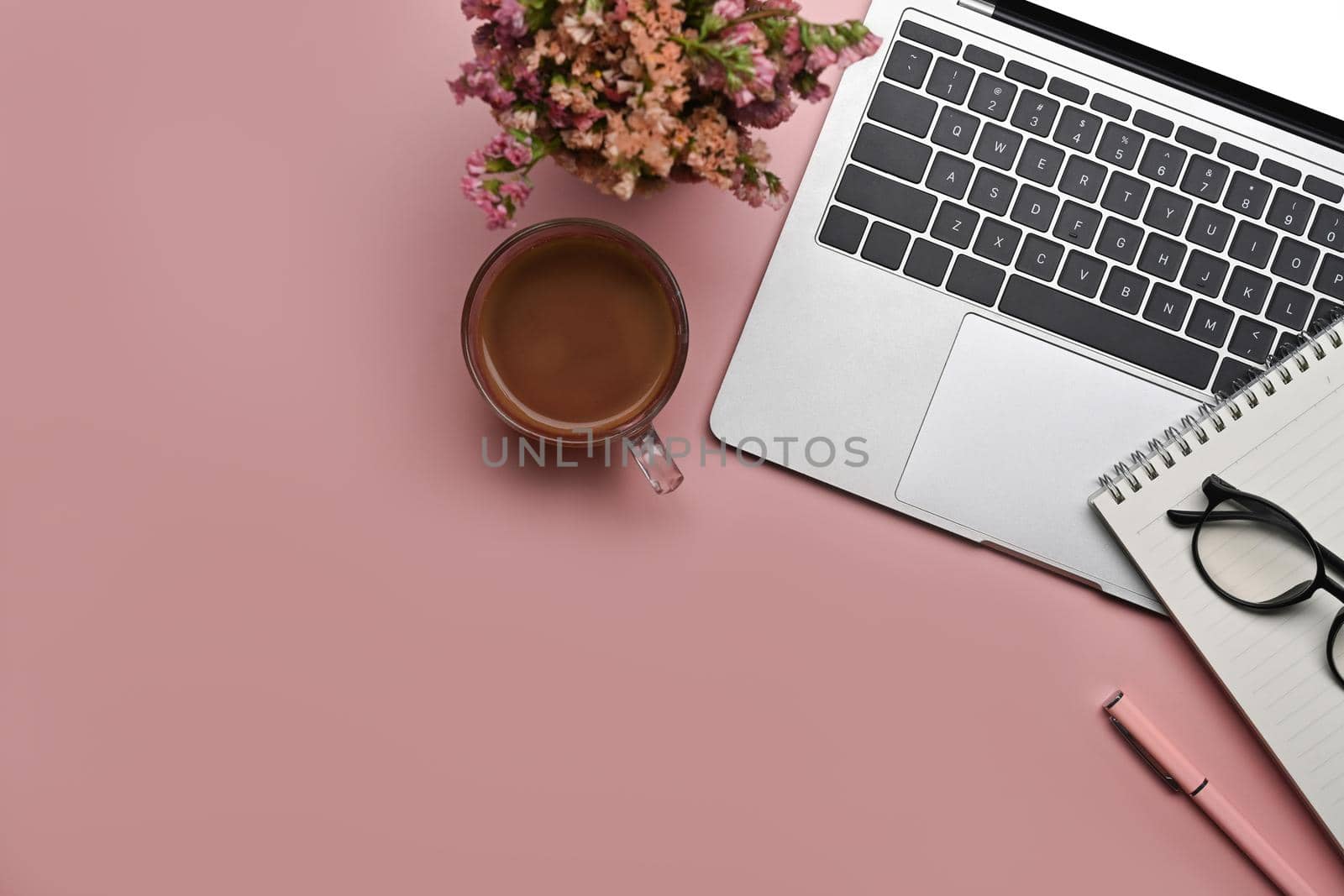 Above view feminine workspace with laptop, notepad, flowers and coffee cup on pink background.