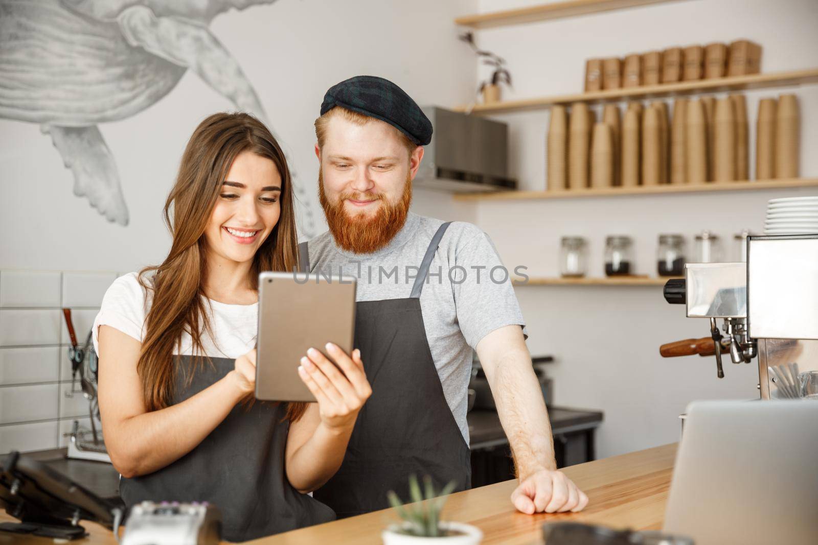 Coffee Business Concept - Satisfied and smile owners couple look on tablet orders online in modern coffee shop