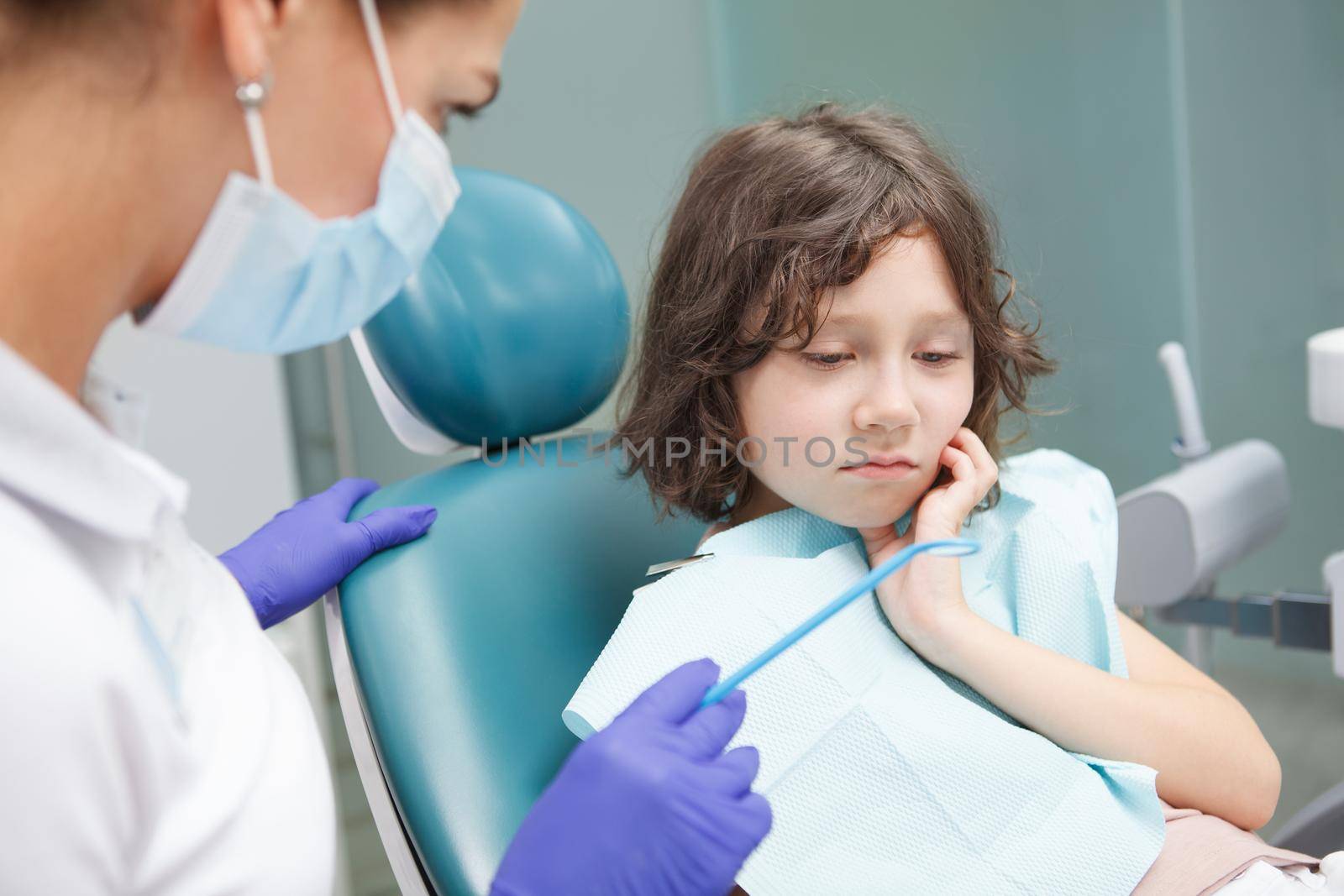 Adorable little boy having toothache, sitting in dental chair at clinic