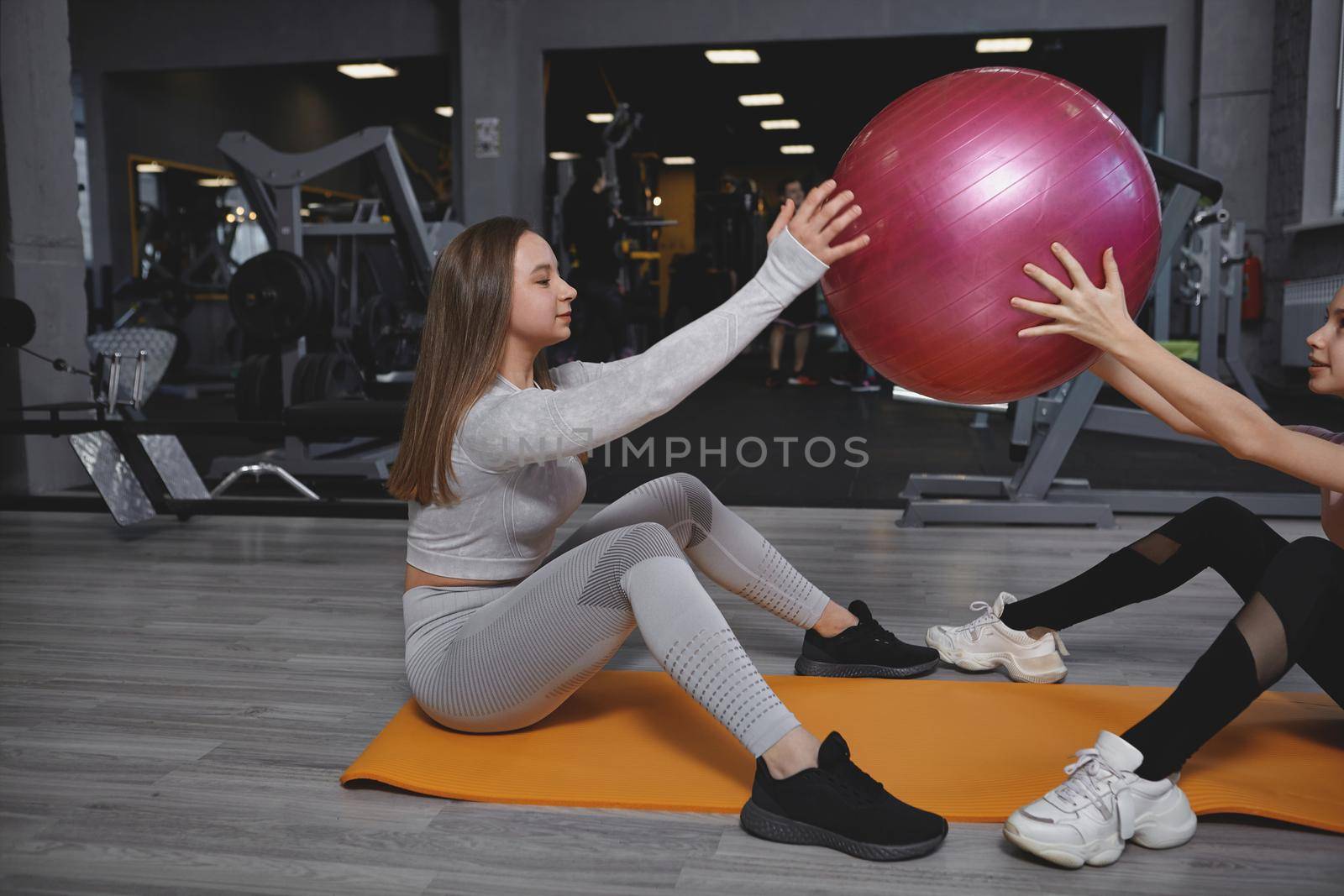 Fitness trainer exercising with her teen client, doing fit ball sit ups