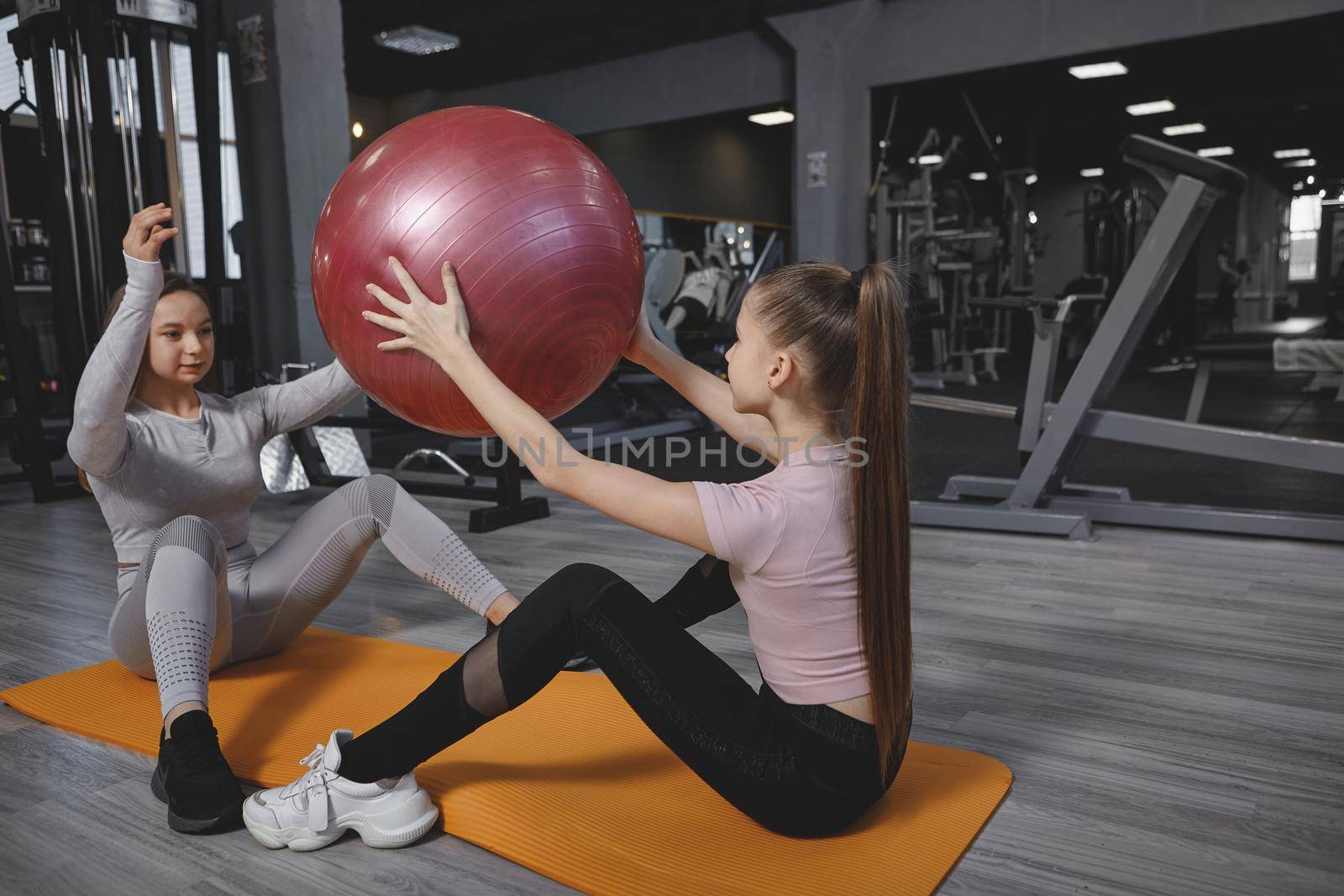 Teenage girl doing situps with fitness ball, exercising with personal trainer at the gym