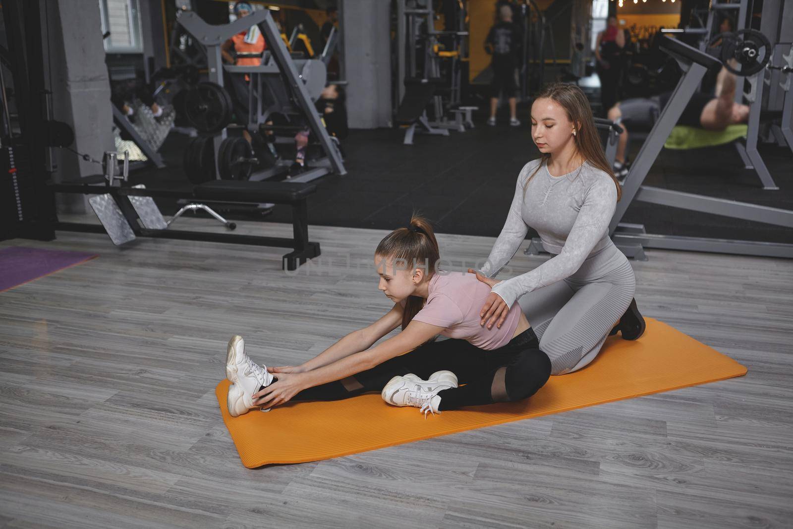 Professional gym coach helping her teen client stretching before workout