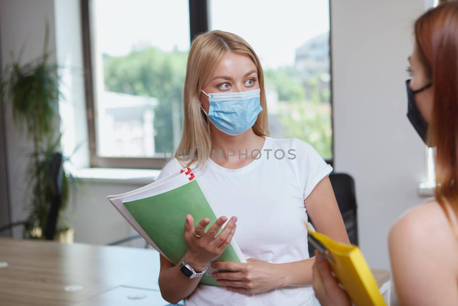 Businesswoman wearing protective face mask, talking to a colleague at the office during coronavirus quarantine
