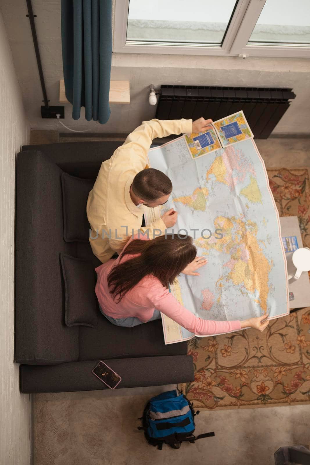 Vertical top view shot of a couple looking at world map choosing next destination for their vacation