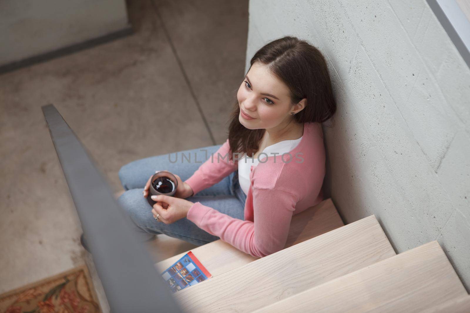 Top view shot of a beautiful young woman relaxing sitting on the stairs at her modern apartment, drinking tea