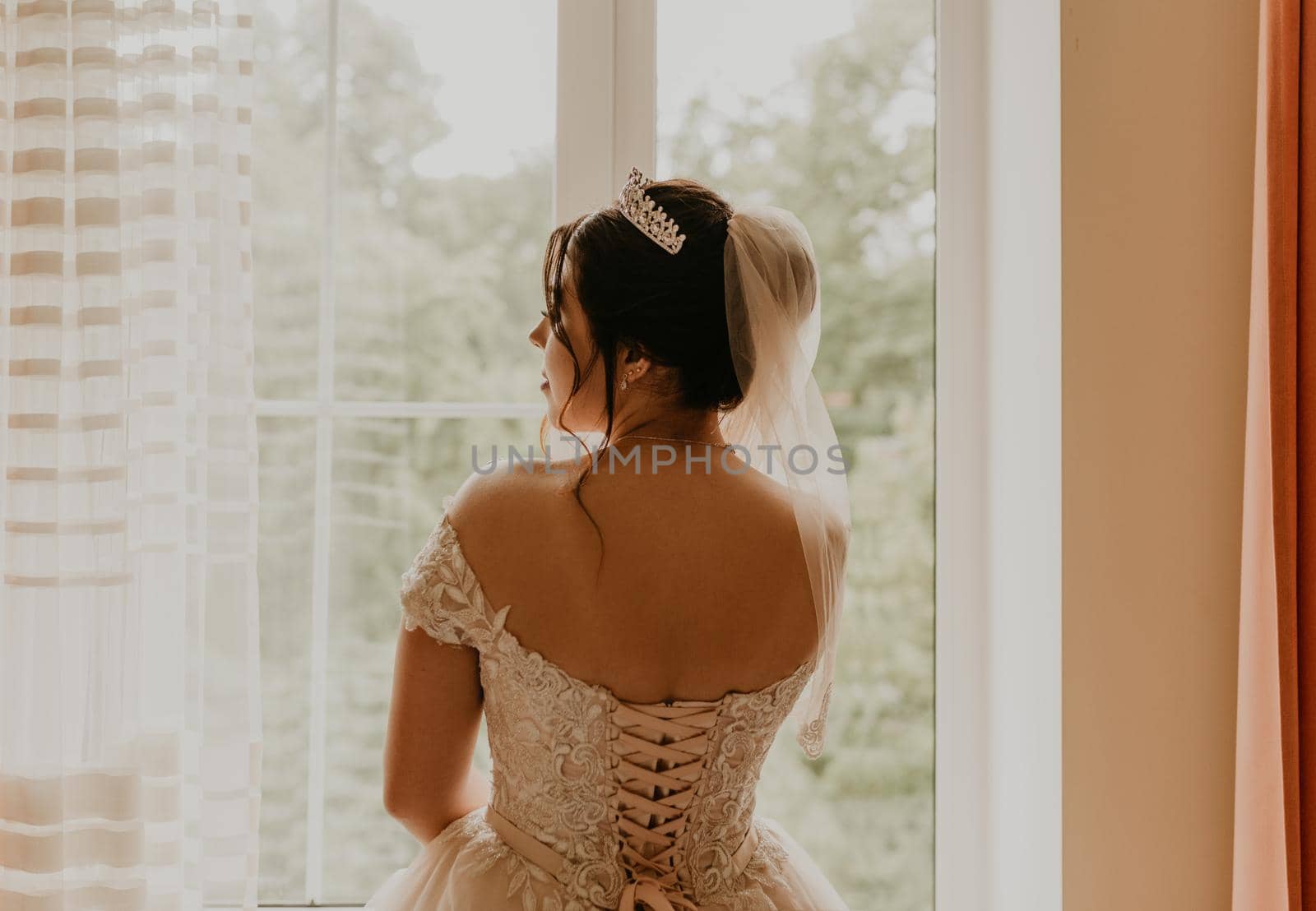 woman bride in white wedding dress girl stands with her back near window morning by AndriiDrachuk